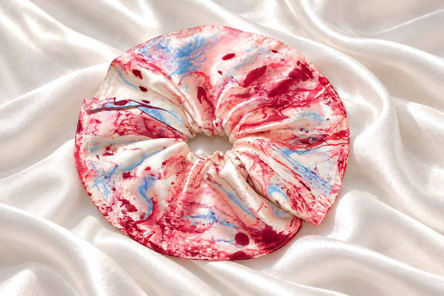 Completed marbled silk scrunchie resting on softly draped white silk